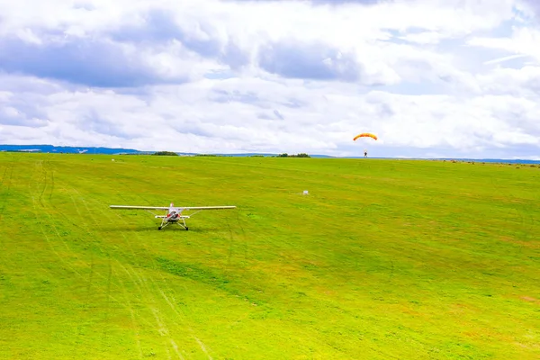 Small plane on a green field, paratrooper landing on a green field. Air entertainment. View from above.