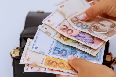 Croatian kunas of different denominations are held by a woman against the background of a bag.
