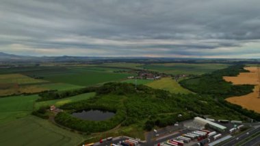 Parking for trucks and cars and a gas station near the green fields and the lake. Cars are driving on the highway. View from above.