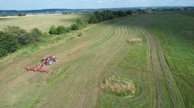 Çiftçi traktöre bağlı bir saman tırmığıyla çimleri çevirir. Yüksekten ateş edilmiş..