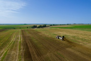 Top view of a tractor scattering manure from a trailer in the field. Fertilizing the soil before plowing. Natural fertilizer.
