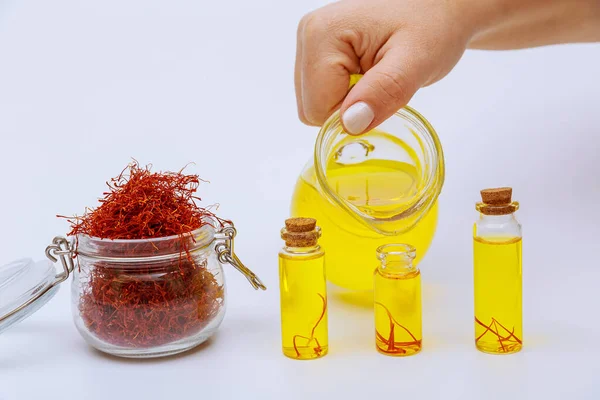 A woman pours a saffron drink into small jars. Saffron tea and a full jar of dry red stamens on a white background.