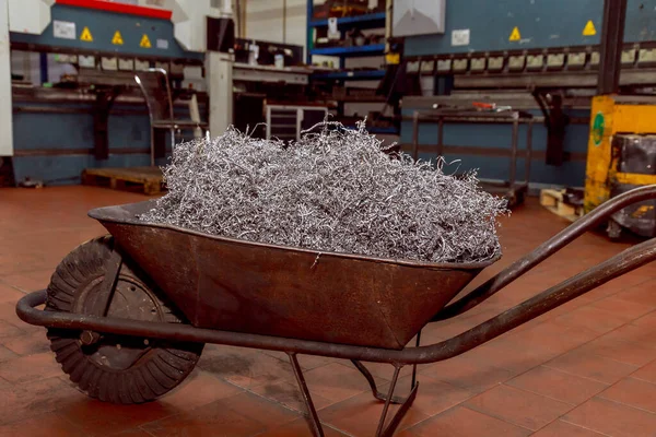 Metal shavings or scrap steel waste in a wheelbarrow at a factory