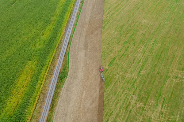 Top view of a tractor plowing the land near the railway and a corn field. Season of work on the field. Agriculture.