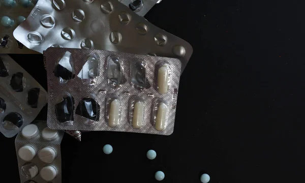 Tabletten und Pillen auf schwarzem Hintergrund, geöffnete Pillenverpackungen, zerknüllte Pillenverpackungen — Stockfoto