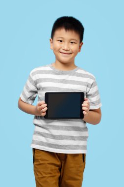 Çocuk elinde tabletle gülümsüyor, mavi arka planda tişört giyiyor.