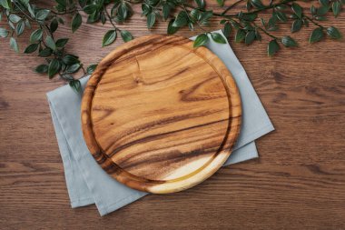 Koyu ahşap masa arkasında mavi peçeteli ahşap tabak, pizza tabağı, kesim tahtası.