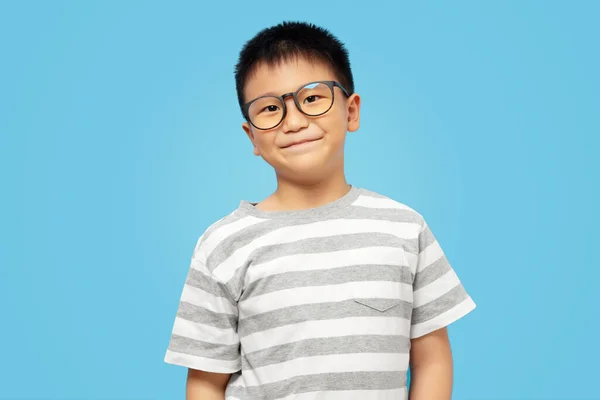 Inteligentny Dzieciak Uśmiechem Noszący Okulary Koszulkę Patrzący Kamerę Niebieskim Tle — Zdjęcie stockowe