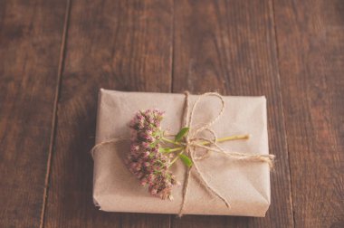 Kravat kağıdına sarılı ev yapımı hediyeler ve ahşap bir masada pembe çiçekler. Çiçeklerle süslenmiş güzel hediye kutusunun yakın plan resmi