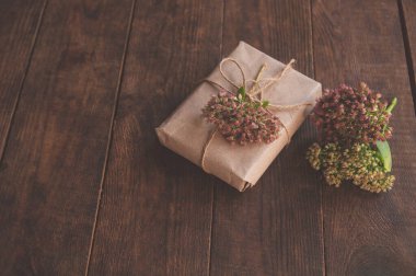 Kravat kağıdına sarılı ev yapımı hediyeler ve ahşap bir masada pembe çiçekler. Çiçeklerle süslenmiş güzel hediye kutusunun yakın plan resmi