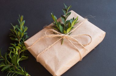 Siyah arka planda yeşil yaprakları olan doğal düğümlü bir hediye kutusu. Esmer arka planda indirim kavramı