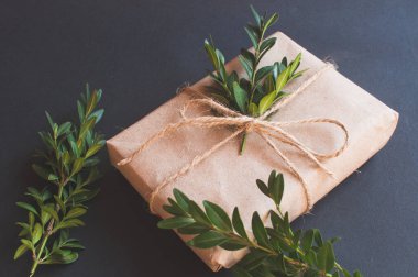 Siyah arka planda yeşil yaprakları olan doğal düğümlü bir hediye kutusu. Esmer arka planda indirim kavramı