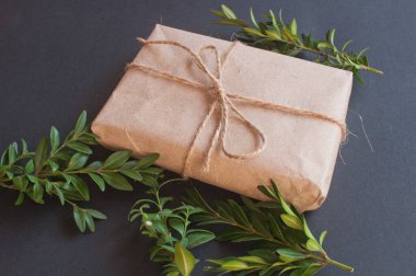 Siyah arka planda yeşil yaprakları olan doğal düğümlü bir hediye kutusu. Esmer arka planda indirim kavramı