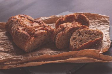 Siyah arkaplanda mayasız buğday ekmeği, kağıt üzerinde dilimlenmiş ekmek.