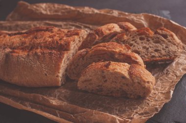 Siyah arkaplanda mayasız buğday ekmeği, kağıt üzerinde dilimlenmiş ekmek.