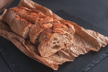 tahıl ekmeği siyah arkaplanda parşömen kağıdında parçalara ayrılmış.