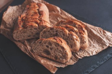 tahıl ekmeği siyah arkaplanda parşömen kağıdında parçalara ayrılmış.