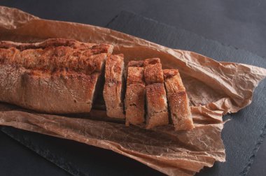 tahıl ekmeği siyah arkaplanda parşömen kağıdında parçalara ayrılmış.