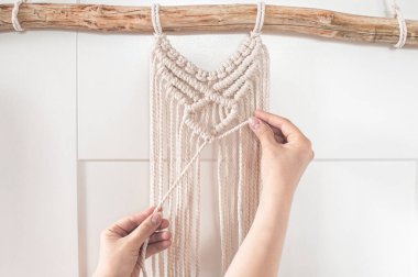 Kız, büyük bir duvar paneli için doğal beyaz pamuk ipliklerinden makrome desenler örüyor.