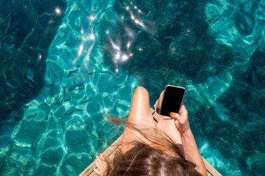 Deniz kenarındaki cep telefonu ekranına dokunan kadın.