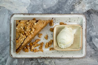 Bir dilim cevizli kek ve dondurma mermer zeminde porselen servis tabağında