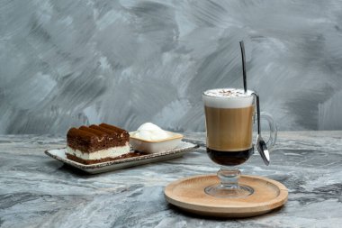 Bir fincan kahve ve mermer zeminde bir dilim tiramisu tatlısı.