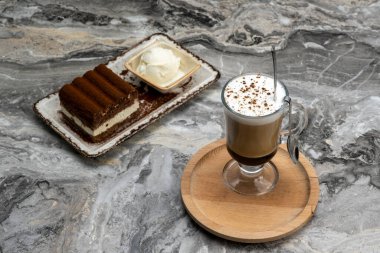 Bir fincan kahve ve mermer zeminde bir dilim tiramisu tatlısı.