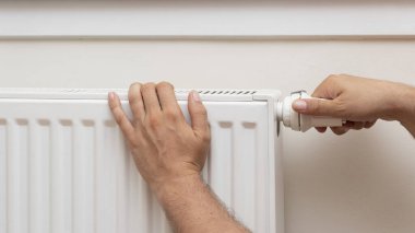 Man's hand adjusting the temperature of a radiator. front view