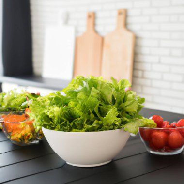 Fresh vegetables and salad bowls on kitchen wooden counter, front view