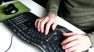 Avrupalı bir adam evdeki ofis masasındaki bir e-postayı, ergonomik klavye ve beyaz masadaki ergonomik fareyi modern ekipman ve ev konseptinden verimli bir iş çıkarmak için zarif periferikler olarak kullanıyor.