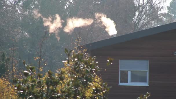 冬のブロックハウスの喫煙煙突煙と都市バンガローの屋根の牧歌的な田舎で白い煙と寒い季節に暖房のための冬の煙の雲を示しています — ストック動画