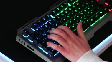 Aydınlatılmış masaüstü pc 'de bilgisayar oyunları oynayan genç, eğlence etkinliği oyuncuları için elektronik ekipman ve multimedya pazarı ile esportları ve video oyunu rekabetini gösteren bulanık bir arkaplan olarak oynuyor