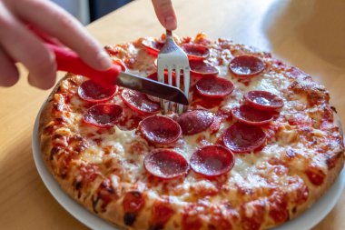 Oğlan elleri salam pizzasını çatal ve bıçakla parçalara ayırır pizza tabağında yakın çekim macro manzaralı lezzetli peynirli ve salamlı aç gençler için sağlıksız yağlı fast food olarak İtalyan leziz diyeti