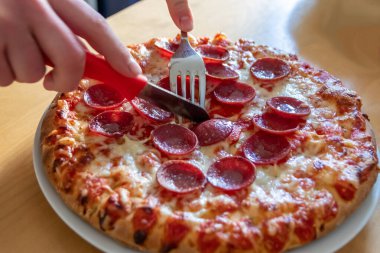 Oğlan elleri salam pizzasını çatal ve bıçakla parçalara ayırır pizza tabağında yakın çekim macro manzaralı lezzetli peynirli ve salamlı aç gençler için sağlıksız yağlı fast food olarak İtalyan leziz diyeti