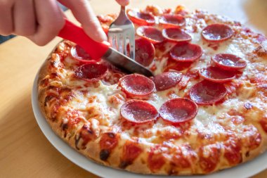 Oğlan elleri salam pizzasını çatal ve bıçakla parçalara ayırır pizza tabağında yakın çekim macro manzaralı lezzetli peynirli ve salamlı aç gençler için sağlıksız yağlı fast food olarak İtalyan leziz diyeti