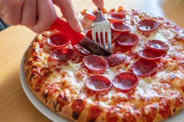 Oğlan elleri salam pizzasını çatal ve bıçakla parçalara ayırır pizza tabağında yakın çekim macro manzaralı lezzetli peynirli ve salamlı aç gençler için sağlıksız yağlı fast food olarak İtalyan leziz diyeti