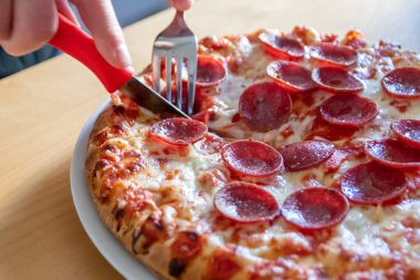 Oğlan elleri salam pizzasını çatal ve bıçakla parçalara ayırır pizza tabağında yakın çekim macro manzaralı lezzetli peynirli ve salamlı aç gençler için sağlıksız yağlı fast food olarak İtalyan leziz diyeti