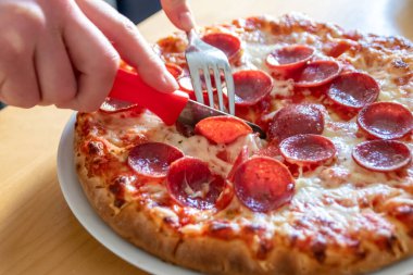 Oğlan elleri salam pizzasını çatal ve bıçakla parçalara ayırır pizza tabağında yakın çekim macro manzaralı lezzetli peynirli ve salamlı aç gençler için sağlıksız yağlı fast food olarak İtalyan leziz diyeti