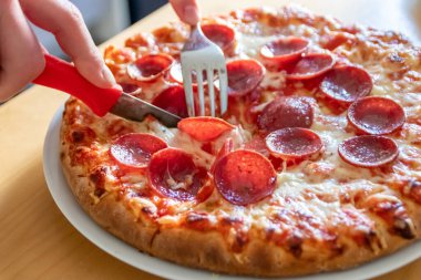 Oğlan elleri salam pizzasını çatal ve bıçakla parçalara ayırır pizza tabağında yakın çekim macro manzaralı lezzetli peynirli ve salamlı aç gençler için sağlıksız yağlı fast food olarak İtalyan leziz diyeti