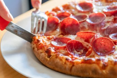 Oğlan elleri salam pizzasını çatal ve bıçakla parçalara ayırır pizza tabağında yakın çekim macro manzaralı lezzetli peynirli ve salamlı aç gençler için sağlıksız yağlı fast food olarak İtalyan leziz diyeti