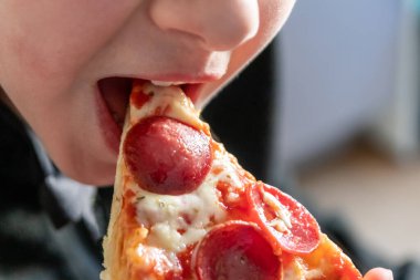 Çocuk eli sıcak buharlı ve lezzetli peynirli pizza salamını tutuyor. Makro görüntüdeki İtalyan lezzetini diyet fast food yemekleri için kalorili sağlıksız bir aperatif olarak görüyor.