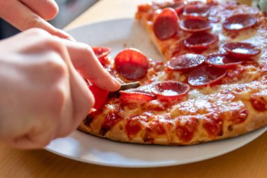 Oğlan elleri salam pizzasını çatal ve bıçakla parçalara ayırır pizza tabağında yakın çekim macro manzaralı lezzetli peynirli ve salamlı aç gençler için sağlıksız yağlı fast food olarak İtalyan leziz diyeti