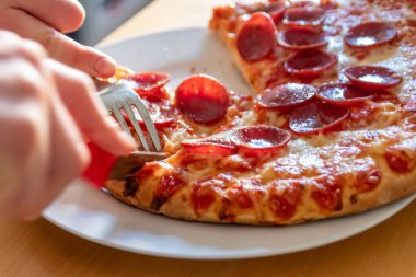 Oğlan elleri salam pizzasını çatal ve bıçakla parçalara ayırır pizza tabağında yakın çekim macro manzaralı lezzetli peynirli ve salamlı aç gençler için sağlıksız yağlı fast food olarak İtalyan leziz diyeti