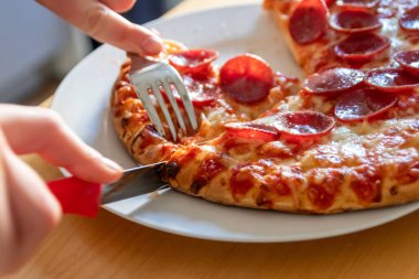 Oğlan elleri salam pizzasını çatal ve bıçakla parçalara ayırır pizza tabağında yakın çekim macro manzaralı lezzetli peynirli ve salamlı aç gençler için sağlıksız yağlı fast food olarak İtalyan leziz diyeti