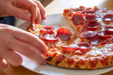 Çocuk eli sıcak buharlı ve lezzetli peynirli pizza salamını tutuyor. Makro görüntüdeki İtalyan lezzetini diyet fast food yemekleri için kalorili sağlıksız bir aperatif olarak görüyor.