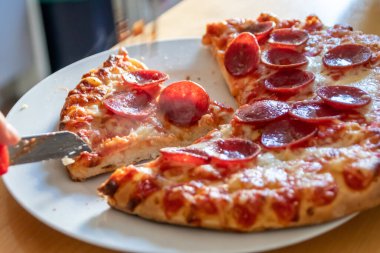 Oğlan elleri salam pizzasını çatal ve bıçakla parçalara ayırır pizza tabağında yakın çekim macro manzaralı lezzetli peynirli ve salamlı aç gençler için sağlıksız yağlı fast food olarak İtalyan leziz diyeti