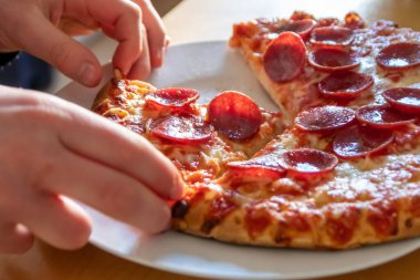 Çocuk eli sıcak buharlı ve lezzetli peynirli pizza salamını tutuyor. Makro görüntüdeki İtalyan lezzetini diyet fast food yemekleri için kalorili sağlıksız bir aperatif olarak görüyor.