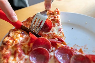 Oğlan elleri salam pizzasını çatal ve bıçakla parçalara ayırır pizza tabağında yakın çekim macro manzaralı lezzetli peynirli ve salamlı aç gençler için sağlıksız yağlı fast food olarak İtalyan leziz diyeti