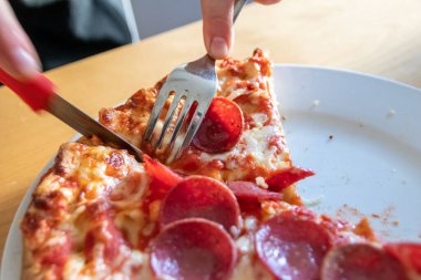 Oğlan elleri salam pizzasını çatal ve bıçakla parçalara ayırır pizza tabağında yakın çekim macro manzaralı lezzetli peynirli ve salamlı aç gençler için sağlıksız yağlı fast food olarak İtalyan leziz diyeti