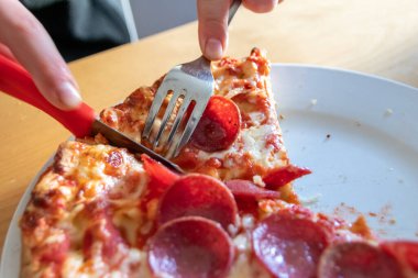 Oğlan elleri salam pizzasını çatal ve bıçakla parçalara ayırır pizza tabağında yakın çekim macro manzaralı lezzetli peynirli ve salamlı aç gençler için sağlıksız yağlı fast food olarak İtalyan leziz diyeti